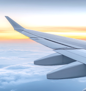An Engineered Components Company airplane wing seen from a window above a layer of clouds at sunset.