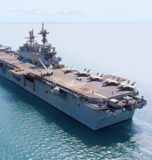 An aerial view of an amphibious assault ship, featuring Engineered Components Company parts, at sea with fighter aircraft parked on its flight deck.